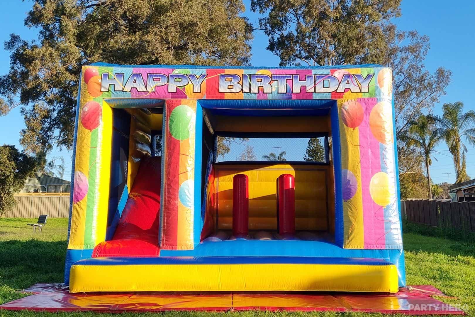 Happy Birthday combo castle with a red slide set up in a park
