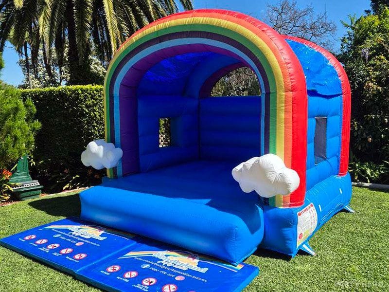 Blue rainbow cloud bounce castle with an arched rainbow roof on a garden lawn