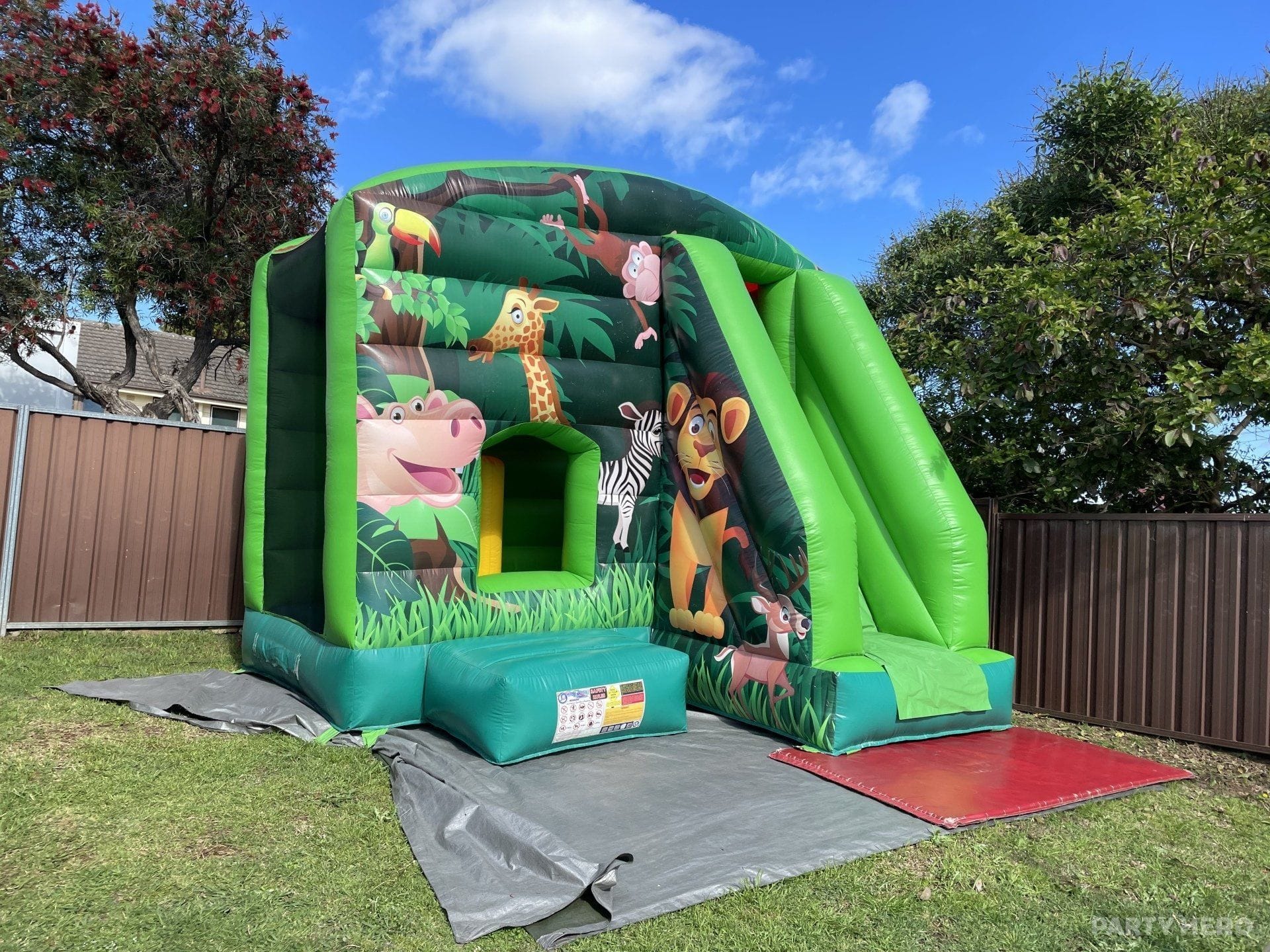 Jungle animal combo castle with a green slide on a backyard lawn