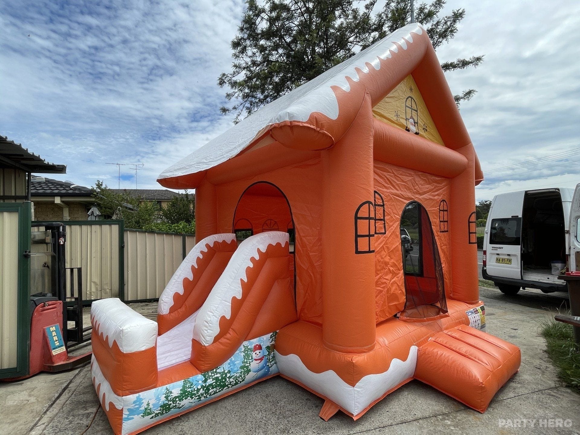 Orange cottage jumping castle with a slide set up beside a driveway