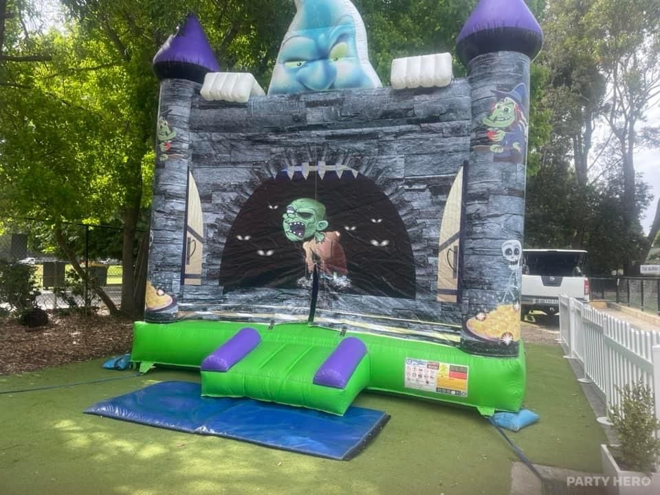 Grey stone castle-themed jumping castle with a green bounce floor on grass