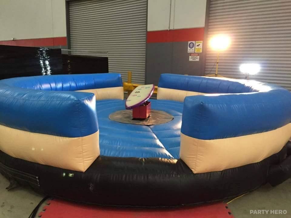 Mechanical surfboard ride inside a blue and cream inflatable surround, set up indoors