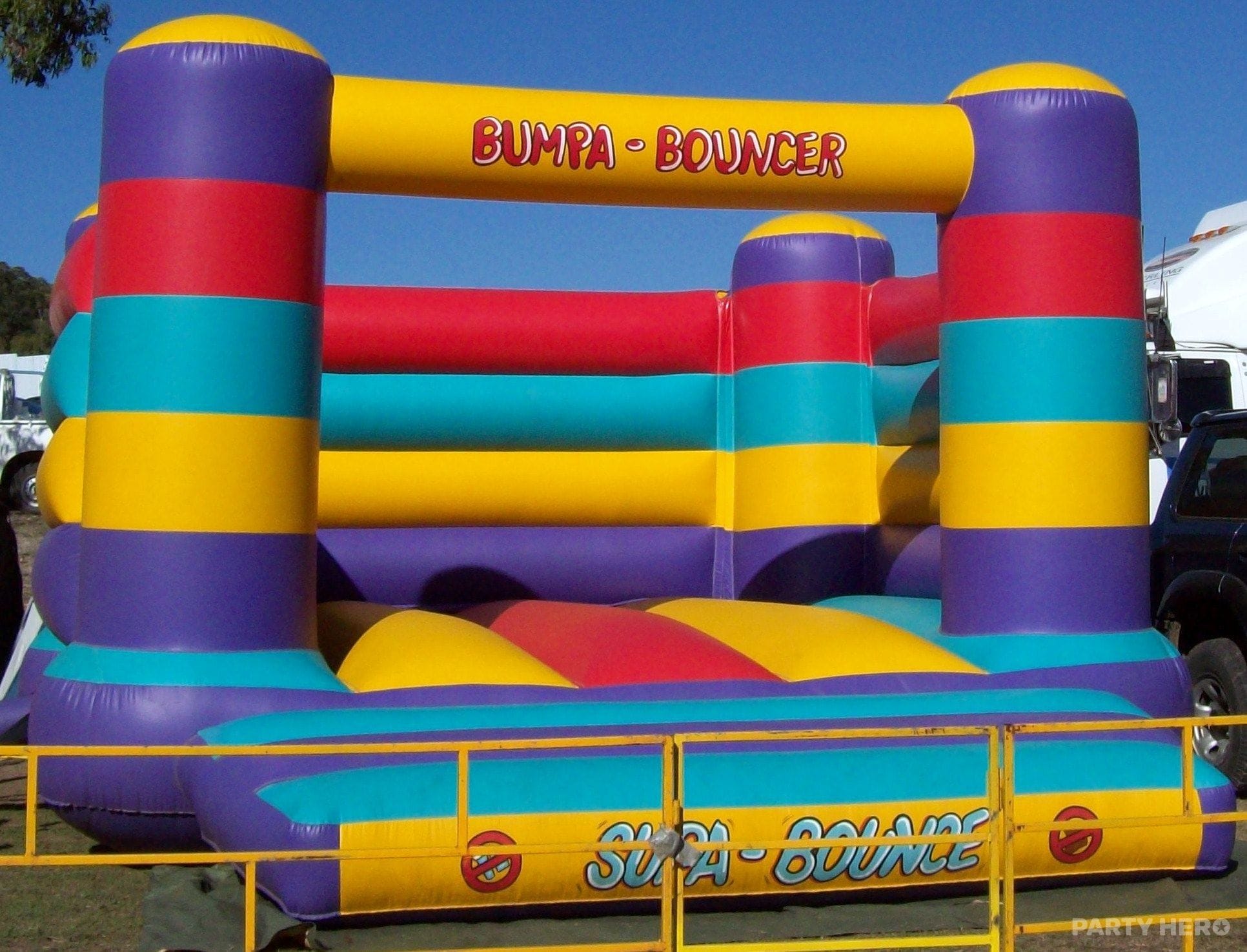 Yellow, purple and teal 6m by 6m jumping castle set up behind safety barriers at an outdoor event in Sydney