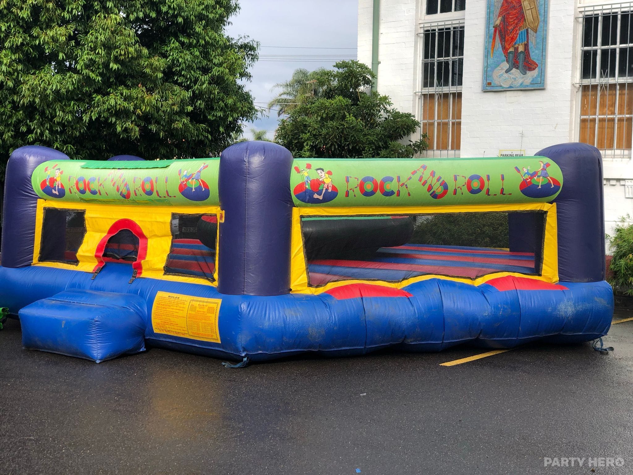 Open-sided rock-and-roll style bouncer with a padded inflatable wall, set up on a driveway
