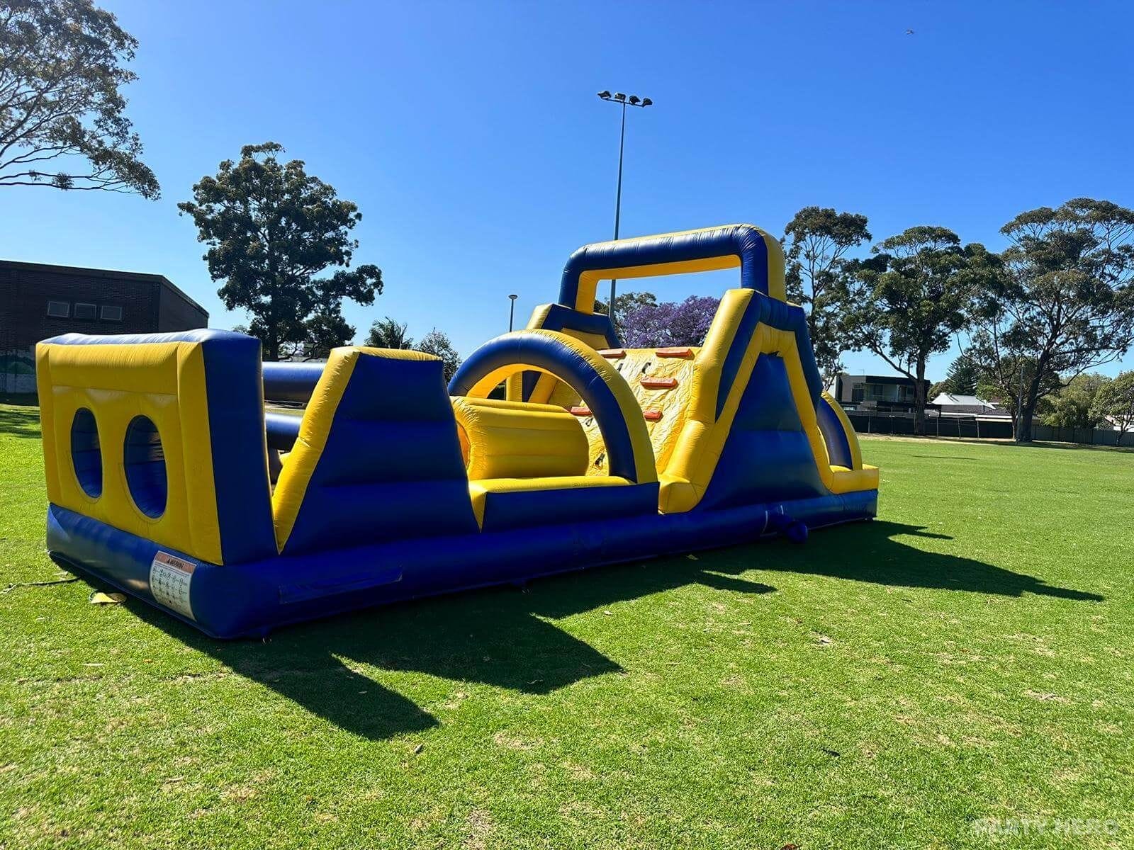 Blue and yellow inflatable obstacle course laid out across a sports oval