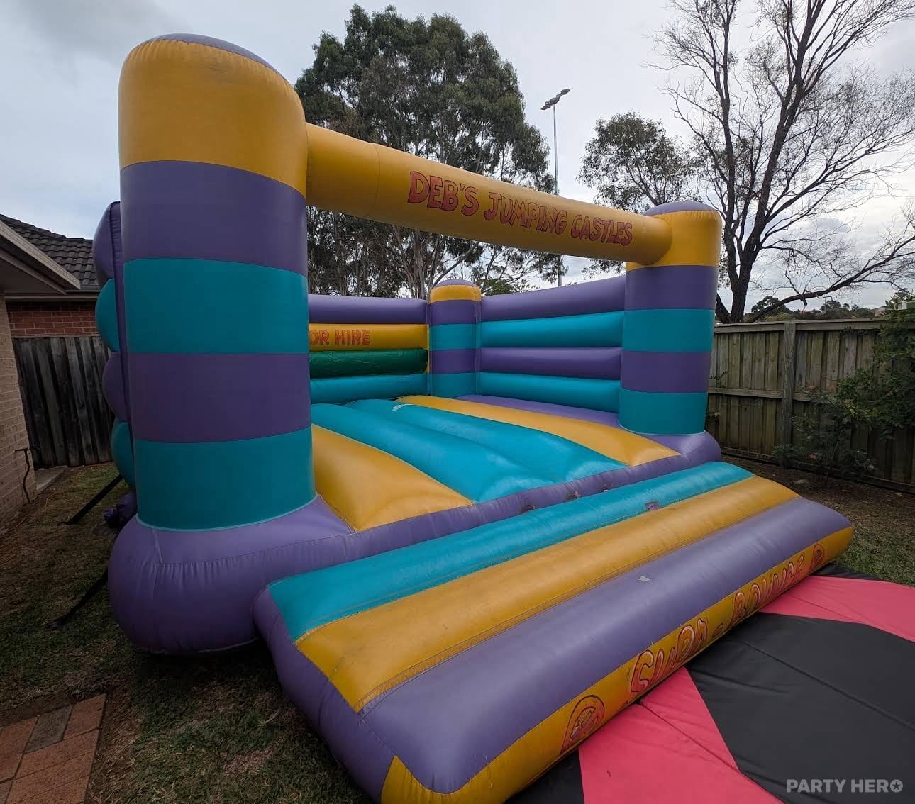 Purple, teal and yellow open bouncing castle set up in a suburban backyard