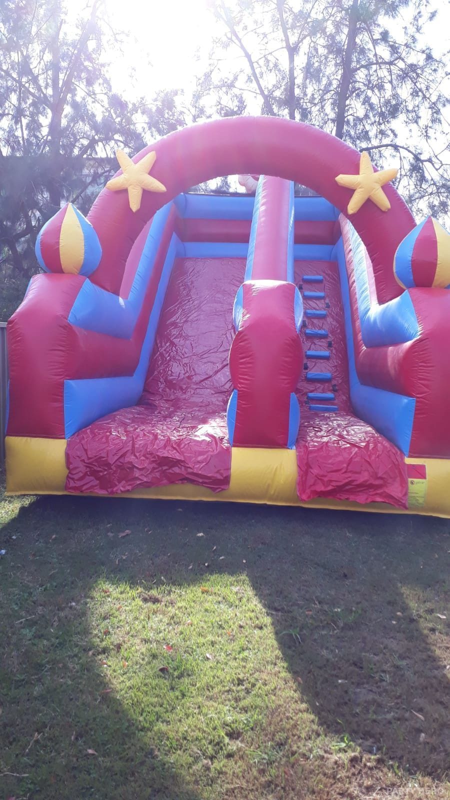 Pink and red inflatable dry slide with climbing steps, inflated on a paved area