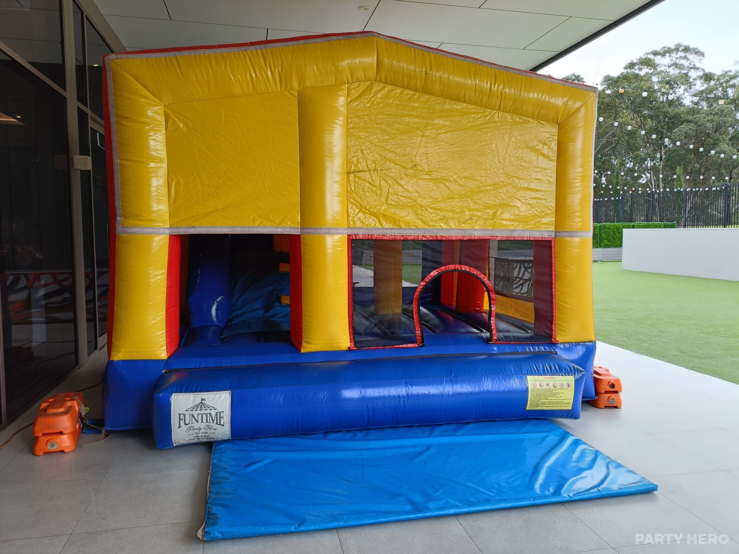 Plain yellow, red and blue jumping castle with no theme, set up on a covered patio with a safety mat