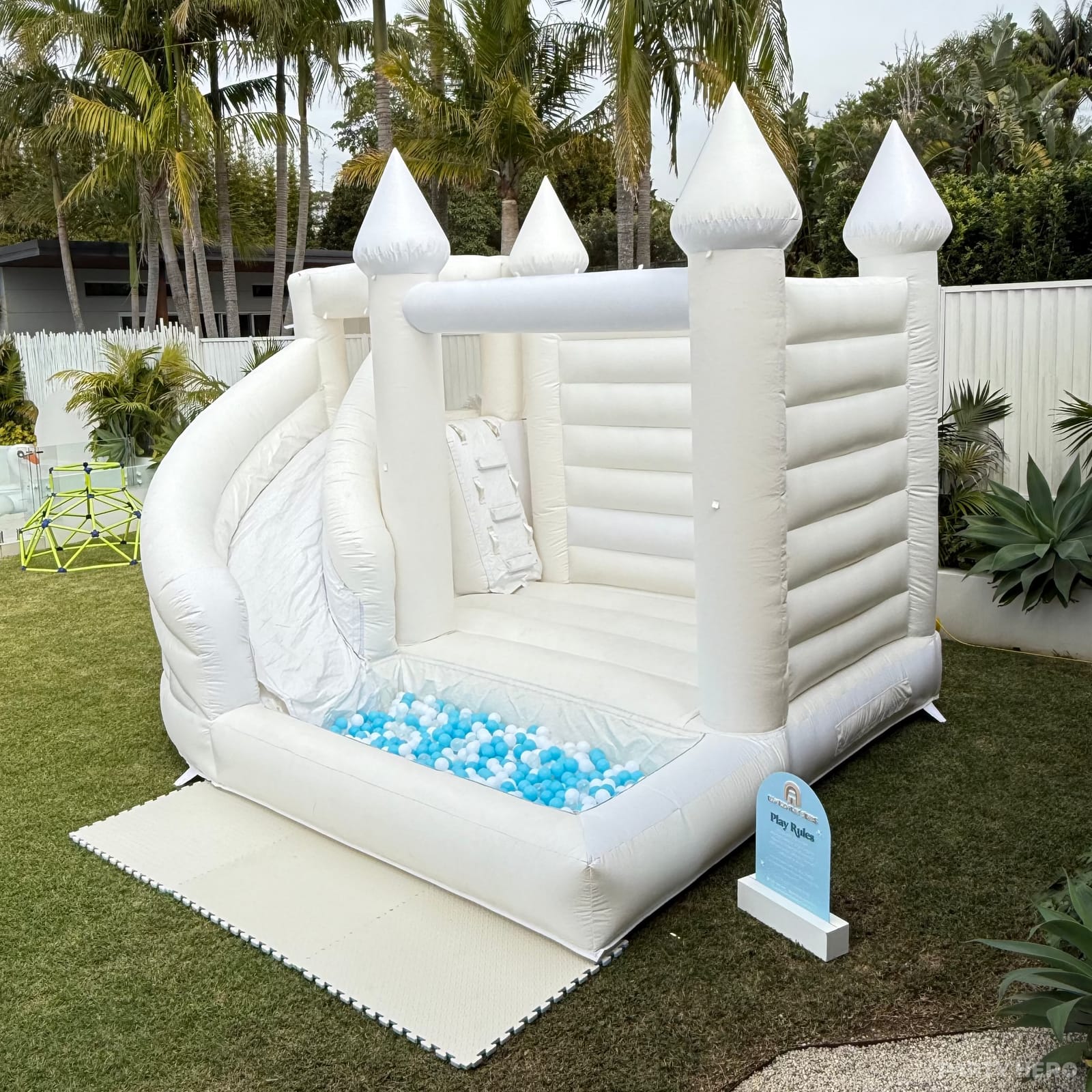 White bounce house with a slide and blue ball pit on a backyard lawn