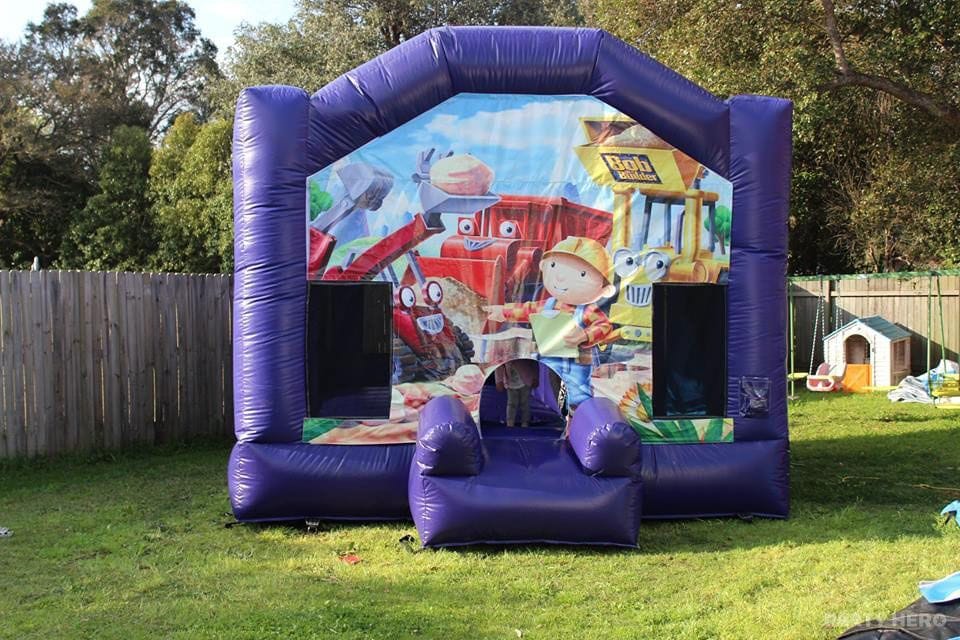 Purple jumping castle with a construction theme set up on grass