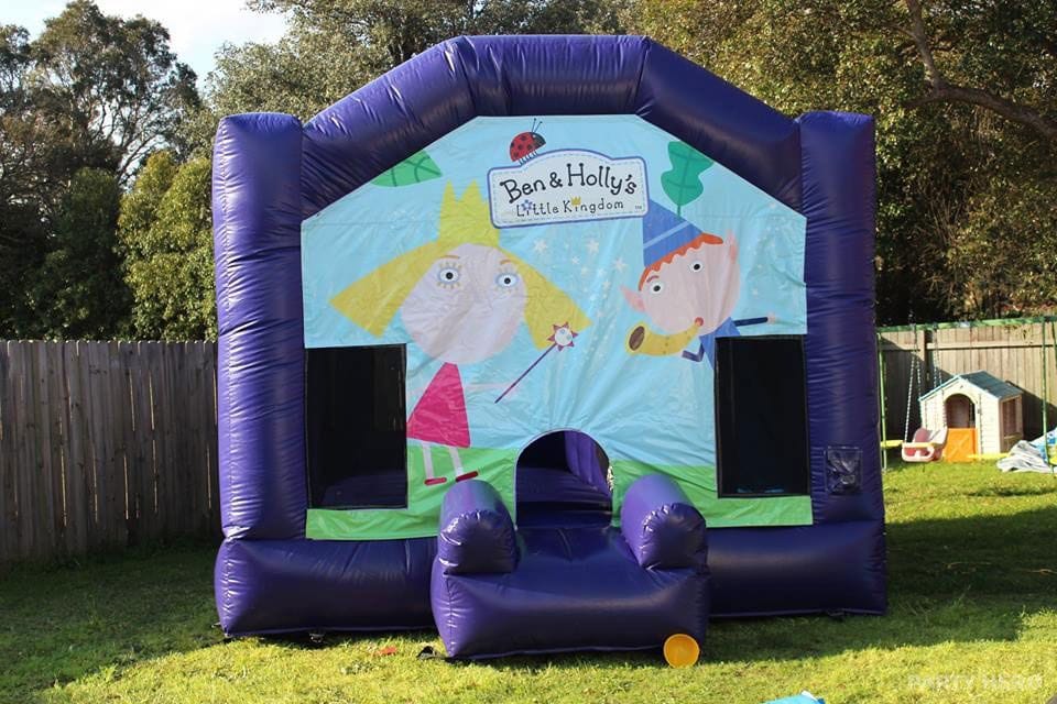 Purple jumping castle with a character banner on a backyard lawn